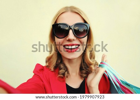 Portrait close up of happy smiling young woman taking a selfie picture by smartphone with shopping bags