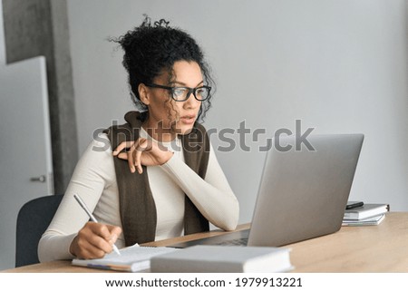 Young adult African American mixed race student wearing glasses watching online webinar on pc writing notes on desk at home modern home office. Remote distant e learning work concept.