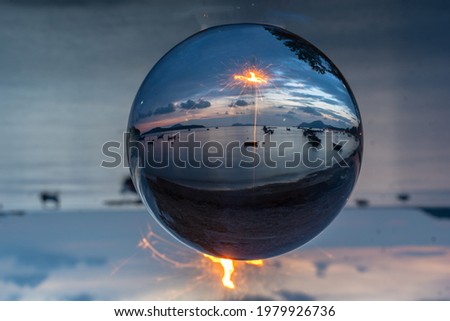 The sparkle of burning steel wool is the red line in the glass ball in twilight. With the sea and the morning light as a background.

