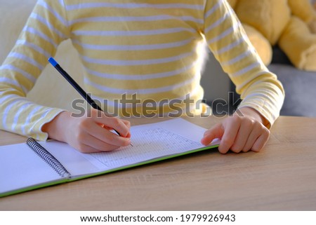 child, schoolboy in yellow t-shirt, writes letters in notebook with an pencil, bright backlight, education concept, hand development, developing writing skills, learning foreign languages