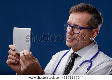Doctor wearing a stethoscope looking at a handheld digital tablet with thoughtful expression in a medical technology and healthcare concept