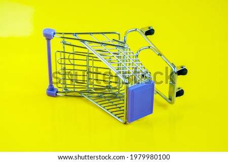 An iron empty grocery cart on a yellow background, turned on its side