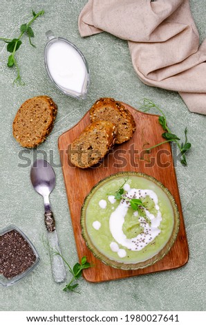 Thick cream soup of green vegetables with white sauce, chia seeds and pea sprouts on a green background. Selective focus.