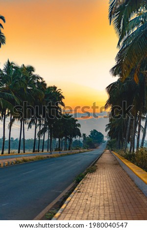A long road with clouds during Sunrise. This picture clicked in 2020 in Goa. Early morning on the time of Sunrise. Golden hour, Orange light and these tones. An empty road