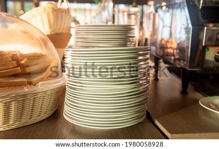 Stacked of white ceramics plate for bread slices on the wooden table in the restaurant. Selective focus.