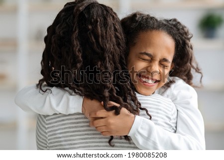 Ecstatic african american school girl with curly hair hugging her mother with eyes closed, closeup portrait, copy space. Adorable black family young woman and her daughter embracing