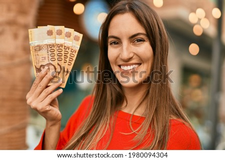 Young hispanic woman smiling happy holding hungarian forint banknotes at the city.