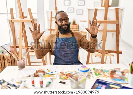 African american artist man at art studio showing and pointing up with fingers number ten while smiling confident and happy. 