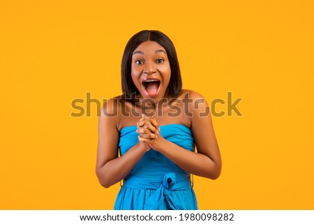 Overjoyed black lady shouting OMG, clasping her hands together, excited over huge summer sale on orange studio background. Young African American woman in trendy outfit screaming WOW