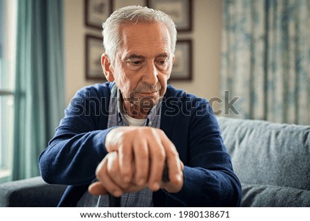 Depressed old man sitting at home while holding walking stick. Retired sad man holding wooden walking cane handle sitting alone at care facility. Elderly man suffering from loneliness and alzheimer. Royalty-Free Stock Photo #1980138671