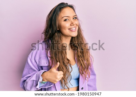 Young hispanic girl wearing casual clothes doing happy thumbs up gesture with hand. approving expression looking at the camera showing success. 