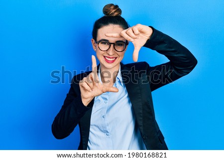 Young hispanic girl wearing business clothes and glasses smiling making frame with hands and fingers with happy face. creativity and photography concept. 