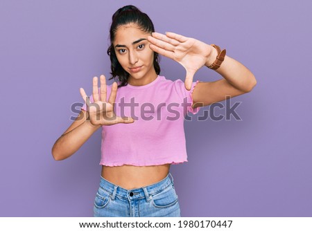 Hispanic teenager girl with dental braces wearing casual clothes doing frame using hands palms and fingers, camera perspective 