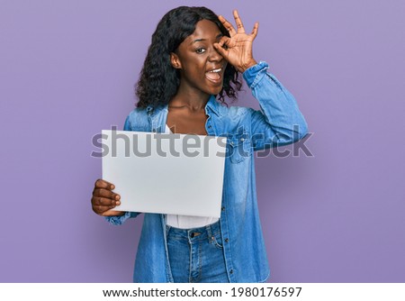 Beautiful african young woman holding blank empty banner smiling happy doing ok sign with hand on eye looking through fingers 