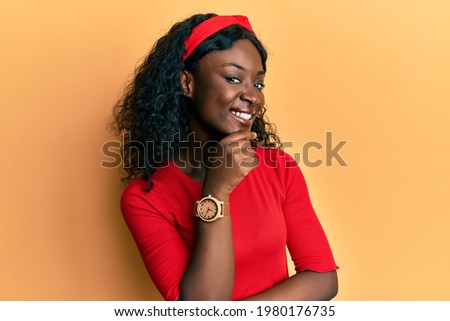 Beautiful african young woman wearing casual clothes smiling looking confident at the camera with crossed arms and hand on chin. thinking positive. 