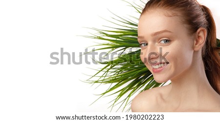 Happy Young Red-Haired Lady Posing With Green Plant Smiling To Camera Advertising Natural Cosmetics Standing Over White Background. Studio Shot, Panorama With Blank Space