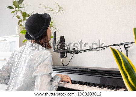 European woman hipster in a hat plays the piano and sings, recording music and song or podcast, woman musician creates audio content, recording voice and music for an audio book or radio show