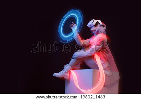Woman with futuristic tablet in hand. Girl in glasses of virtual reality presses the start button. Augmented reality game, future technology, AI concept. Holographic interface to display data. Royalty-Free Stock Photo #1980211463