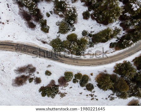 Aerial top view of a spiral road with trees on a snowy mountainside. Travel in mountain at winter