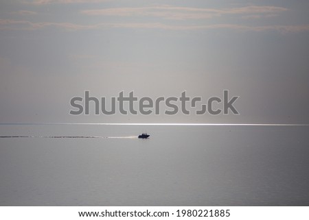 Open sea. A boat is sailing in the distance. The sky almost merges with water. The boat trail is parallel to the horizon. There is copy space.