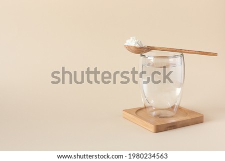 Protein or collagen powder in a spoon and a glass of water on a beige background with a copy space. Extra protein intake. Food supplement concept. Natural beauty and health supplement. Royalty-Free Stock Photo #1980234563