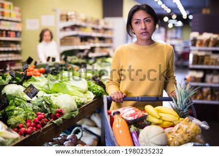 Portrait of positive interested latin american woman visiting supermarket food department for shopping