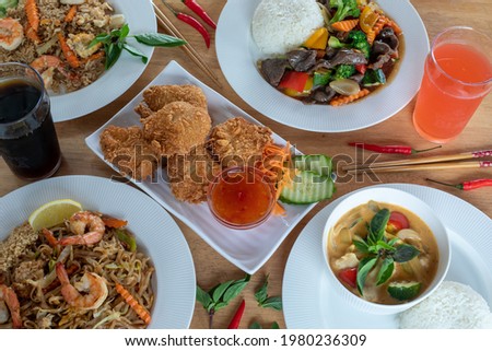 A top-down view of several varieties of Thai food with pares chopsticks in hand with wood background. Bamboo shoots, Glass noodles, Carrot, Oyster sauce, Rice, shrimp, Cabbage, onions, strong basil,