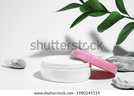 White jar of medicated nourishing and moisturizing face cream with pink lid isolated on white background with plant branch shadow and eco stones. Skin care concept. Copy space Royalty-Free Stock Photo #1980249119
