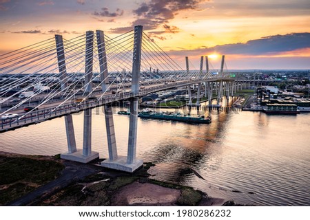 Aerial view of the New Goethals Bridge at sunset, spanning Arthur Kill strait between Elizabeth, New Jersey and Staten Island, New York. A conatiner ship navigates under the bridge. Royalty-Free Stock Photo #1980286232