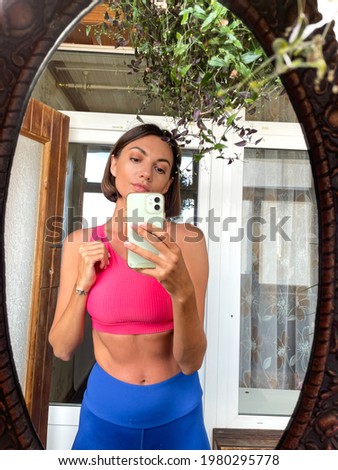 Pretty woman at home take photo selfie in mirror on mobile phone for stories and posts in social media, vertical frame, wearing sport wear, fit and slender, abs motivation