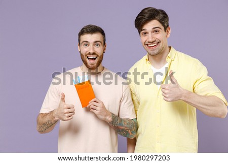 Two traveler tourist men friends in t-shirt hold passport ticket show thumb up tattoo translate fun isolated on purple background. Passenger travel abroad weekend getaway. Air flight journey concept