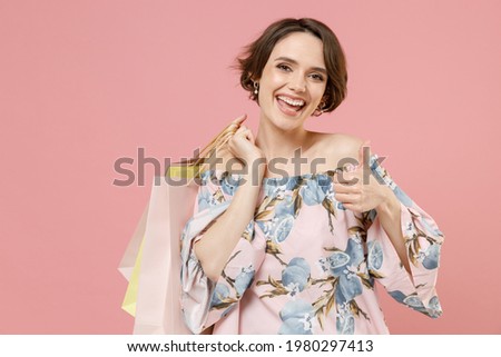 Young excited happy woman 20s with short hairdo wear trendy stylish blouse holding package bags with purchases after shopping show thumb up like gesture isolated on pastel pink color background studio