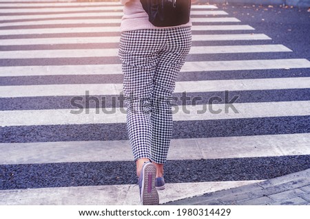Girl crosses the road at a pedestrian crossing. Fashionable woman at the crosswalk makes a step. Young fashionable woman crosses the road on a zebra. Road signs. Rules for walking. Road safety