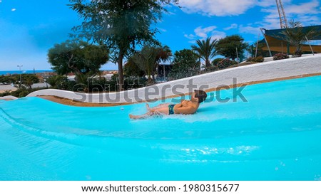 caucasian 8 year old boy lying down and speeding down sliding in a water blue slide at Water Amusement Park on summer in a hot day. Happiness in holidays.