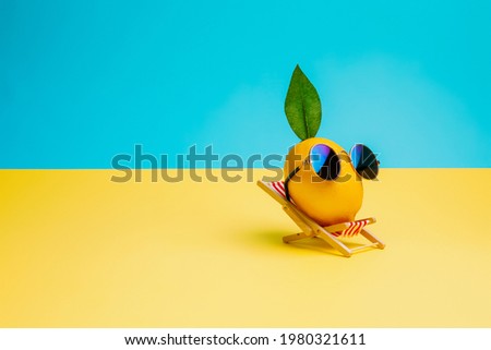 Lemon fruit chilling in beach chair on the blue and yellow background. Summer vacation concept. Sunglasses on lemon with green leaf relaxing on the sunbed. Creative art minimal aesthetic. Royalty-Free Stock Photo #1980321611