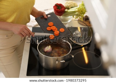 Woman putting carrot into pot to make bouillon in kitchen, closeup. Homemade recipe