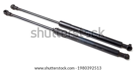 A pair of black metal hood shock absorbers with chrome elements - detail of a car mechanism on a white isolated background. Spare parts for body repair.