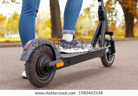 Close up woman legs standing on the electric kick scooter in autumn day back view riding Royalty-Free Stock Photo #1980403148