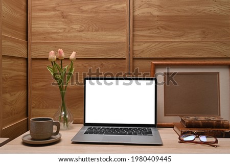 Mock up computer laptop, coffee cup, flowers and empty photo frame on wooden desk.