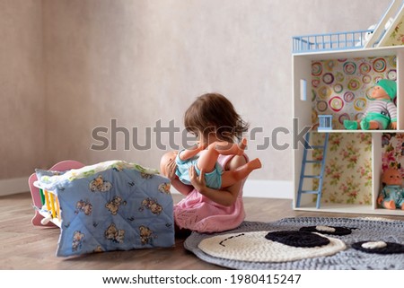 Cute little girl is playing with a doll at home. The child puts the doll to sleep in a toy bed. Role-playing games for children Royalty-Free Stock Photo #1980415247