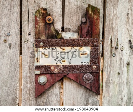 Hand-made guard dog sign and picture made with staples, metal and wood all rusty and discolored on a public fence