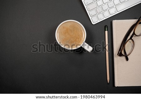 Top view workspace concept. Workspace with, keyboard, glasses, pencil, notepad and coffee mug on black background.