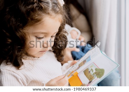 Hispanic toddler girl watching a picture book with her mom-Little girl learning to read