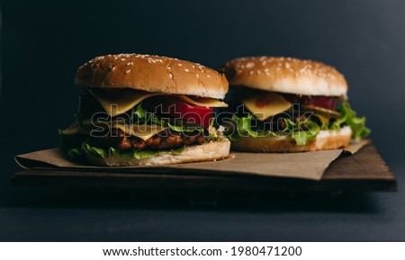 Delicious big juicy burger with tomatoes, cucumbers, cabbage, greens, cheese, cutlet on a gray background. Two sandwiches, fast food. Snack, appetizing, bun with sesame seeds. Serving in restaurant