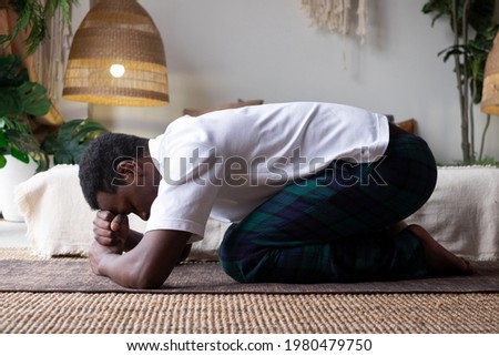 African man doing yoga at home, having rest in balasana or child pose, relaxing body muscles between asana