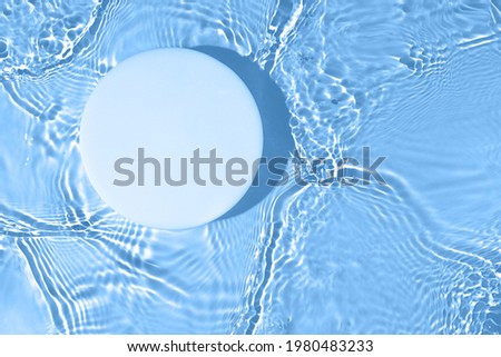 Empty white circle podium on transparent clear calm blue water texture with splashes and waves in sunlight. Abstract nature background for product presentation. Flat lay cosmetic mockup, copy space.