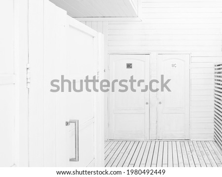 Interior of public outdoors toilet. White wooden walls of water closet on beach. Silver signs on doors of restrooms.
