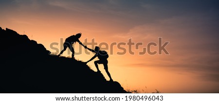 Two people helping each other climb up a mountain. Giving a helping hand,  and adventurous active lifestyle concept.  Royalty-Free Stock Photo #1980496043