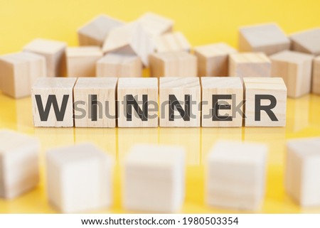 The word winner is written on a wooden cubes structure. Blocks on a bright yellow background. Financial concept. Selective focus. Toy blocks around.