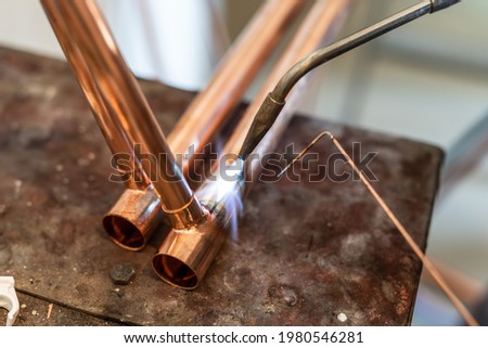 Close up on hands of unknown industrial worker plumber with central heating copper pipes welding using gas torch or blowtorch at work Royalty-Free Stock Photo #1980546281